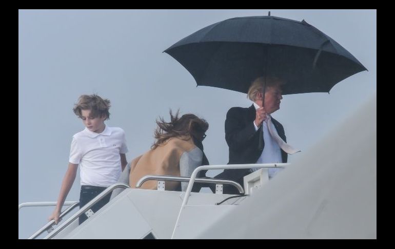 El presidente estadounidense Donald Trump se cubre con un paraguas al momento de abordar el avión presidencial en West Palm Beach, Florida, el 15 de enero, mientras su esposa Melania y a su hijo Barron se mojan. AFP / N. Kamm