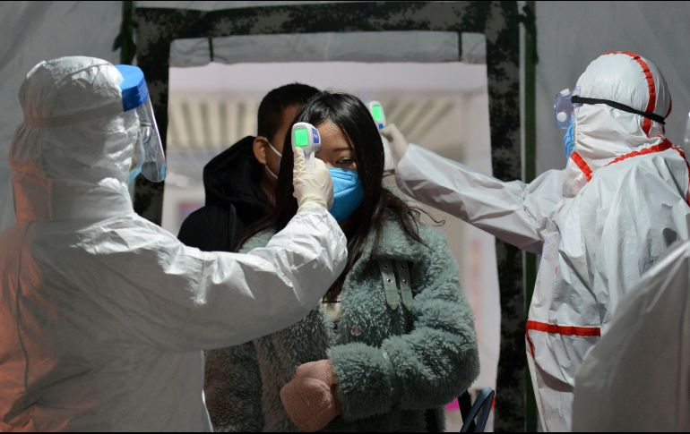 Trabajadores de la salud toman la temperatura a una pasajera en la estación de trenes de Fuyang, China. AP