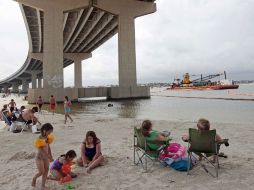 Bañistas toman el sol, mientras un buqeu intenta evitar que el crudo llegue a la costa, en Orange Beach, Alabama. AP  /