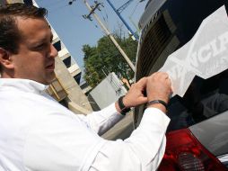 Hernán Cortés Berumen en la pega de calcomanías en un auto, sobre las inmediaciones de la glorieta Minerva. A. HINOJOSA  /