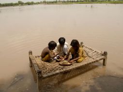 Niños comen sobre la base de una cama en una zona inundada. AP  /