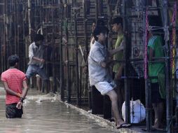 Un hombre se sujeta de una construcción para evitar caer al agua. Calles de Nueva Delhi permanecen inundadas por las lluvias. AP  /