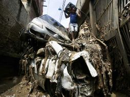 Un hombre intenta pasar por una calle bloqueada por automóviles que fueron arrastrados por las fuertes lluvias que azotaron el país. AP  /