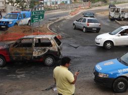 Policías observan la escena donde fueron incendiados tres vehículos en un crucero en Iraja. AFP  /