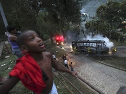Curiosos observan cómo se consume un autobús tras el enfrentamiento entre policías y pandilleros, en Río de Janeiro. AP  /