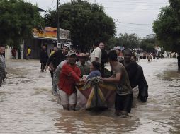 Residentes colombianos ayudan a cruzar a una señora la calle inundada por medio de un bote. AP  /