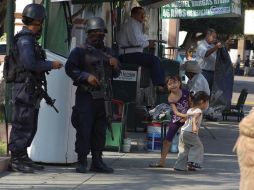 Dos niñas juegan en el Centro de Apatzingán, al lado de dos agentes federales armados. REUTERS  /