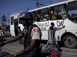 Un haitiano tacha con aerosol las siglas de la ONU ante la desatención de un policía. AP  /