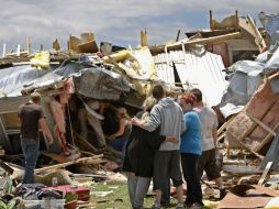 Una familia observa su hogar en ruinas, mientras buscan lo que quedó de sus pertenencias. AP  /