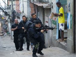 Policías brasileños buscan narcotraficantes, mientras un hombre lee el periódico frente a ellos. AP  /