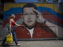 Una mujer camina frente a un portón pintado con la imagen del mandatario sudamericano, en Caracas. AP  /