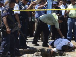 Policías observan el cuerpo de un oficial municipal de Acapulco, asesinado con arma de fuego. AP  /