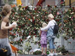 Una mujer consuela a una joven mientras observan una valla revestida con flores. REUTERS  /