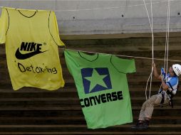 Un activista de Greenpeace cuelga camisetas gigantes de dos conocidas multinacionales textiles en un puente. EFE  /