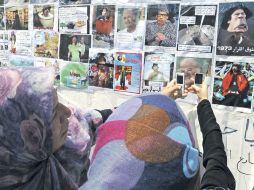 Mujeres toman fotografías con su celular a las imágenes que caricaturizan al ex líder libio. EFE  /