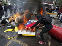 Uno de los manifestantes echa al fuego una bandera chilena. AP  /
