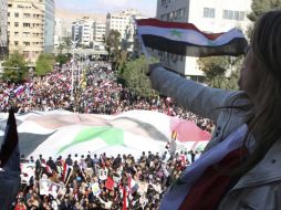 Una mujer ondea una bandera siria desde su balcón mientras una multitud de personas se manifiestan. EFE  /