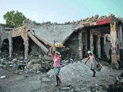 Una mujer pasa frente a una casa destruida por el terremoto hace más de un año. AP  /