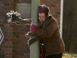 Una mujer tiene que sostenerse de un poste debido a los fuertes vientos en Inglaterra. AP  /