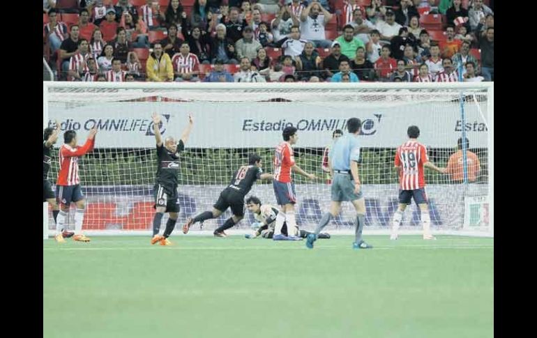 Luis Michel yace en el césped tras haber originado el primer gol de Xolos; Atras, la afición, no lo puede creer.  /