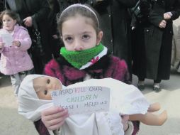 Una niña permanece en las calles con una muñeca y un papel que dice: “Al Assad mata a nuestros niños, por favor ayúdenos”. AP  /