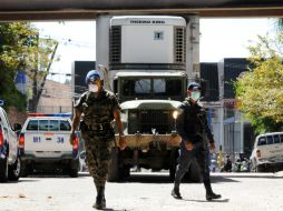 Policías hondureños resguardan la salida de camiones que transportan parte de los cadáveres de las víctimas del incendio. AFP  /