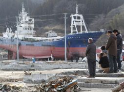 Una familia guarda un minuto de silencio por las víctimas del terremoto de hace un año en Japón, desde el sitio donde vivían. AP  /