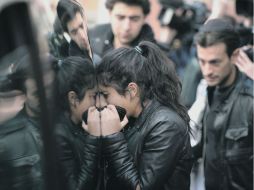 Una mujer llora frente al vidrio de la carroza fúnebre que transporta los cuerpos de los tres niños muertos durante el ataque. AFP  /