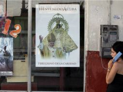 Una mujer usa un teléfono público en Cuba junto a un cartel que anuncia la visita del Papa. AP  /