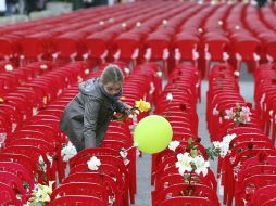 Una niña deja flores sobre algunas de las 11 mil 541 sillas rojas que ocupan la calle principal de Sarajevo. EFE  /