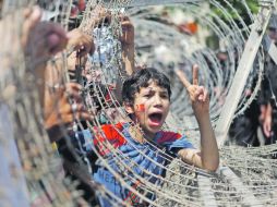 ROSTRO DE LA INSURRECCIÓN. Un niño se asoma a través de un alambrado de púas durante una protesta frente al Tribunal Constitucional. AP  /