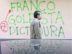 Un hombre camina frente a una barda pintada con un mensaje que califica de “golpista” y “dictadura” al Ejecutivo de Federico Franco. AP  /