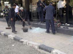 Varios hombres limpian los cristales rotos de una tienda tras una explosión en Damasco. EFE  /
