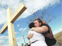 Dos mujeres, deudos de una de las víctimas de los disparos de James Holmes, se abarazan al pie de una cruz de madera. REUTERS  /