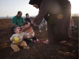 Una refugiada siria tiende su mano hacia unos niños en un campamento de personas desplazadas en la frontera turco-siria. EFE  /