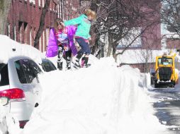 Labores.Unas niñas juegan en un cerro de nieve, mientras una máquina realiza los trabajos de limpieza en Boston,tras la tormenta 'Nemo' AP /
