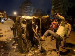 Un hombre golpea a patadas un vehículo después de haber sido incendiado durante la manifestación. AFP /