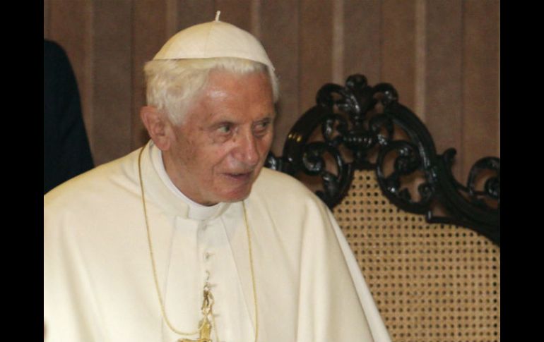 El papa emérito, que viste una gorra blanca y se protege del frío con un abrigo blanco mientras camina ayudado por un bastón. ARCHIVO /