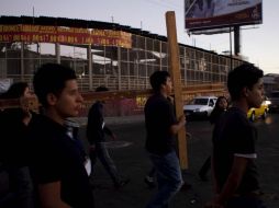 Cuatro hombres jóvenes cargan una cruz de madera. El resto de los fieles los siguen de cerca.  /