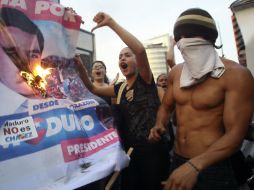 Simpatizantes de Capriles queman un cartel con la imagen de Maduro. Al menos siete personas han muerto por protestas poselectorales. AFP /
