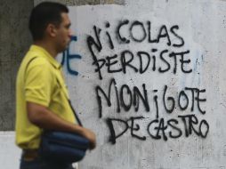 Un hombre camina frente a una pinta en una barda, el texto habla de un suspuesto fraude electoral. AFP /
