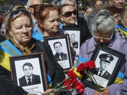 Varias mujeres, que sostienen fotografías de sus maridos y claveles rojos, lloran junto al monumento que recuerda a los fallecidos. EFE /