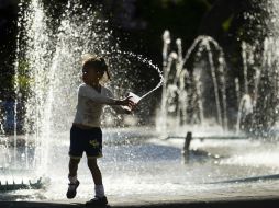 En la imagen, una niña se moja con el agua de una fuente.  /