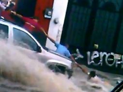 Imangen del video al momento que una cadena de hombres trata de sostener a la persona inmersa en la corriente de agua. ESPECIAL /