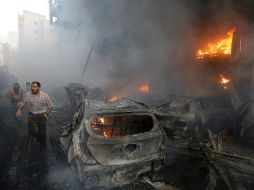 Ciudadanos libaneses corren junto a automóviles quemados a consecuencia de la explosión. AP /