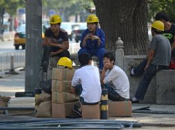 Trabajadores toman un receso en una calle de Beijing. AFP /