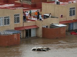 Afectados por la inundaciones miran el nivel del agua desde la azotea de sus casas. AFP /