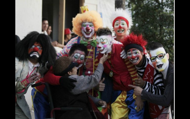 Varios payasos se acercan a una señora, ella acaricia a uno de ellos.  /