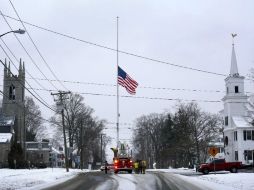 Bomberos colocan a media hasta la bandera estadounidense en la calle principal de Newtown. AP /