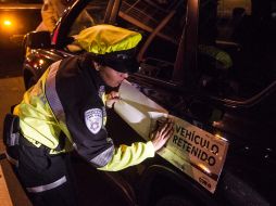 Una oficial de seguridad, pone una calcomanía a un vehículo retenido. ARCHIVO /